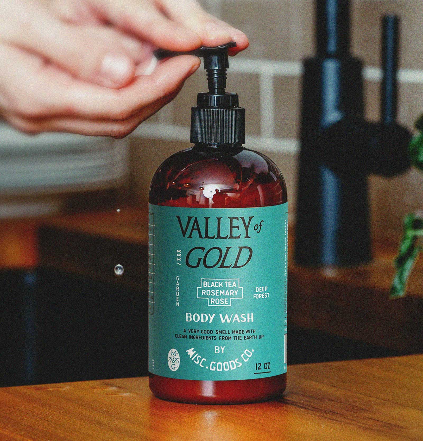 Bottle of Valley of Gold body wash with a pump being pressed on a wooden surface.