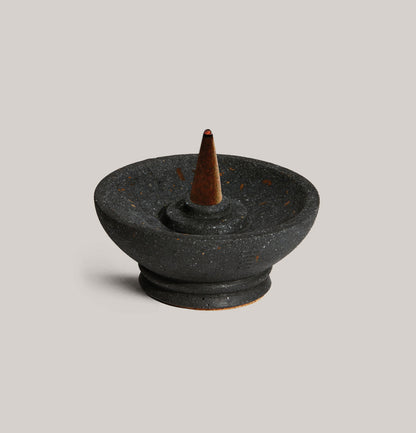 Black ceramic incense burner with a cone on a light gray background