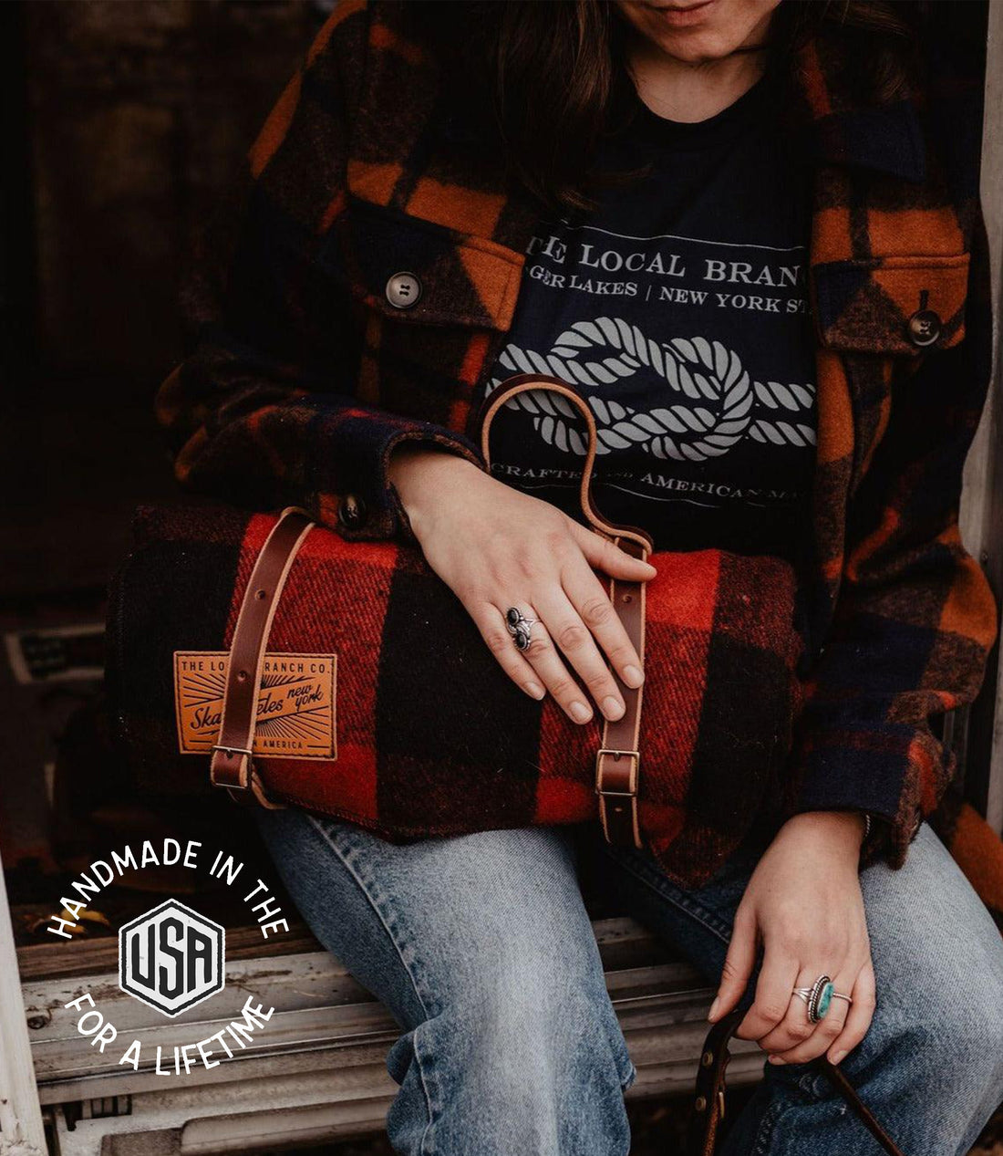 Person wearing a plaid shirt and jeans, holding a brown leather bag with &